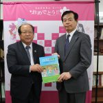 橋本教育長(右)に教材を手渡す長嶋専務